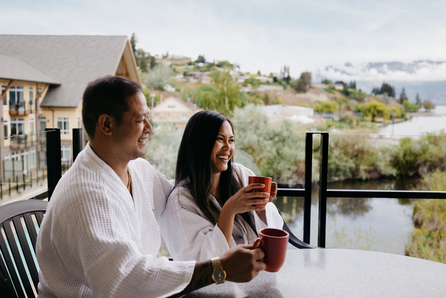 couple sitting on balcony looking at lake with coffee in hand