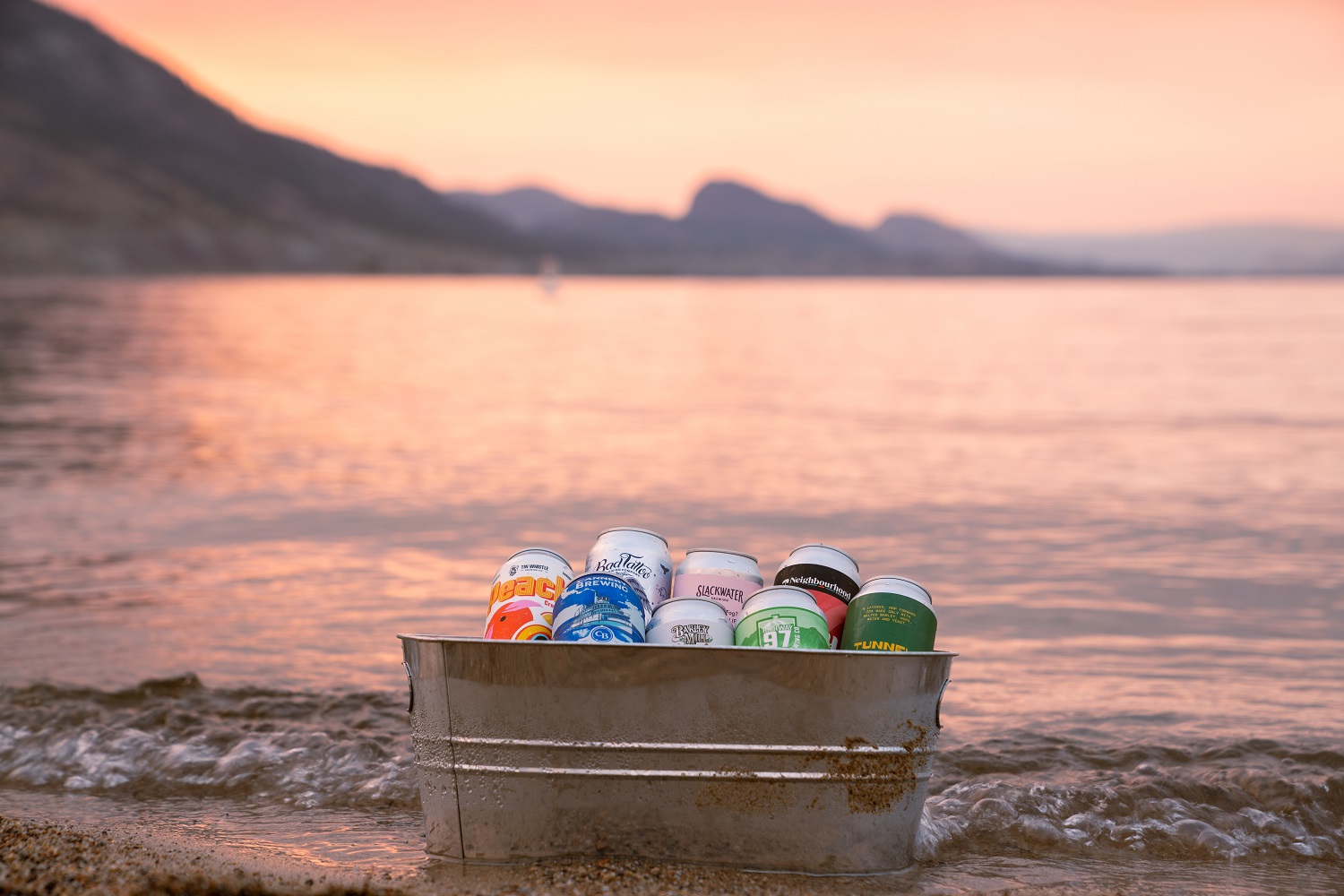 penticton ale trail beers in a bucket on the beach at Okanagan Lake