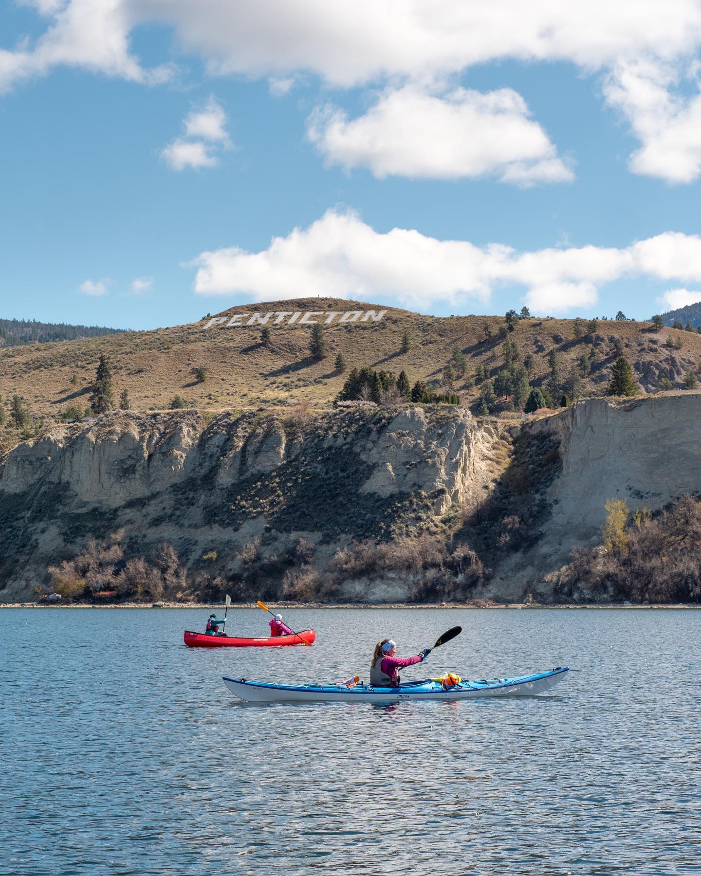 A canoe and a kayak are paddling in front of Munson Mountain on Okanagan Lake