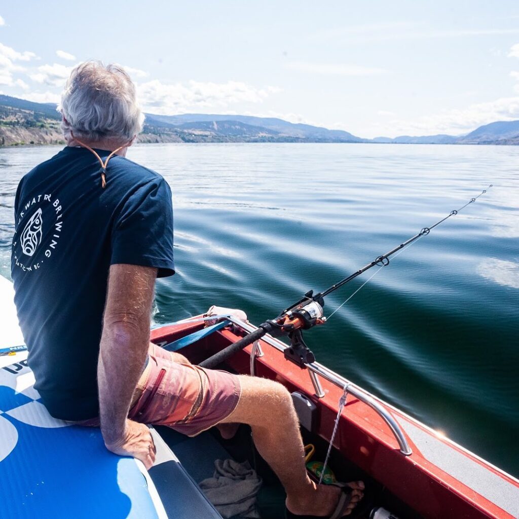 man fishing on Okanagan Lake with a Slackwater t-shirt on