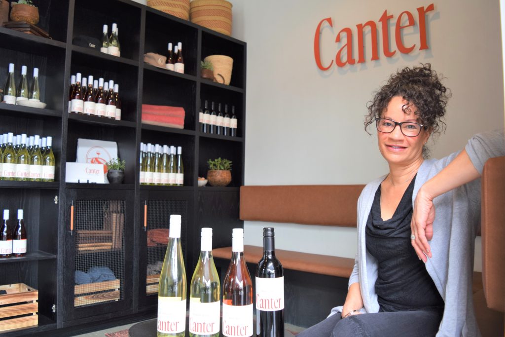 A woman is seen sitting next to four bottles of wine - 2 white, 1 rose, 1 red.

In the background the text 'Canter' is seen on the wall next to a cabinet featuring the wines for sale.