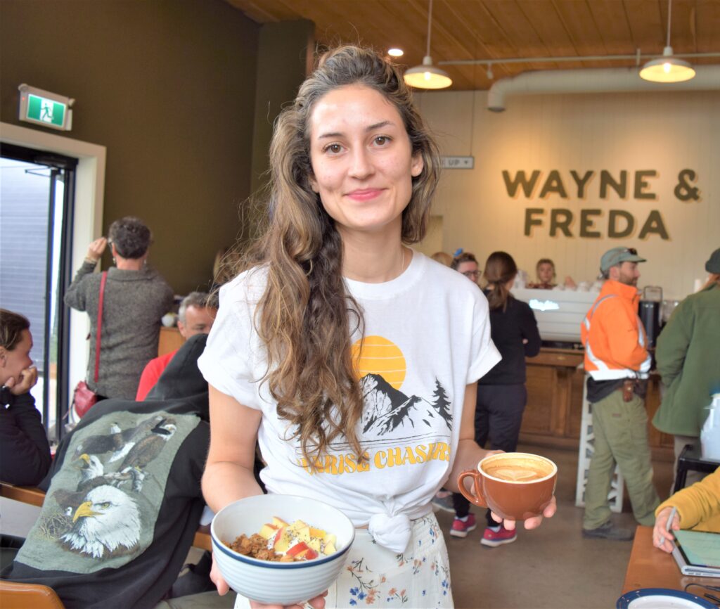 The Manager of Wayne & Freda holding a coffee and a breakfast bowl. 