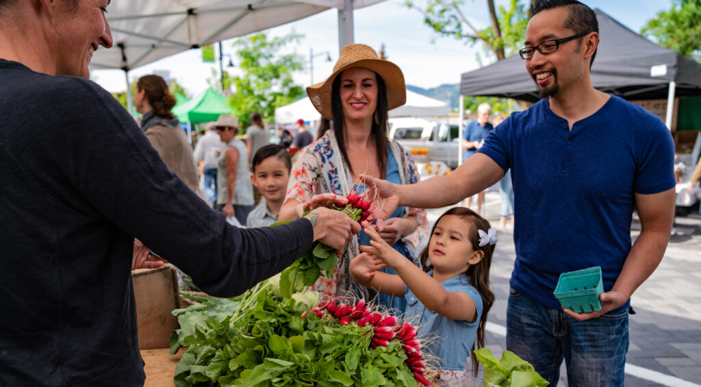 A family of 4 buys radishes from a farmers market vendor. 