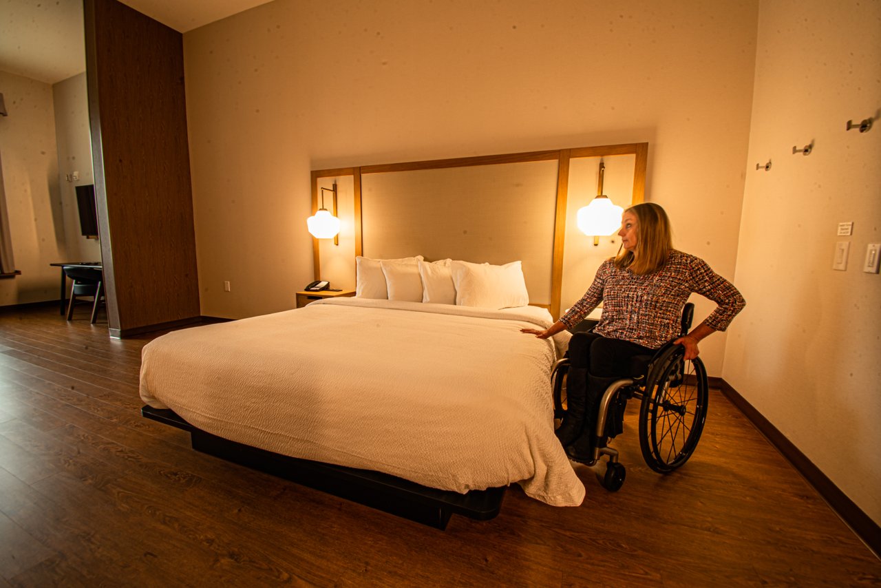 Accessible Tourism - wheelchair user beside an accessible bed at fairfield inn penticton in their accessible room